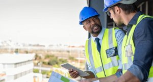 Construction workers talking about new construction site with copy space. Engineers in mechanical factory reading instructions. Architect in construction uniform holding blueprint and discussing.